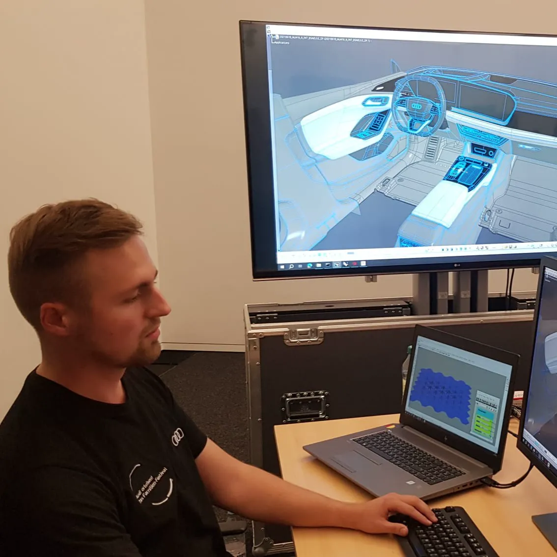 Christian Rauscher sitzt vor einem Bildschirm an einem Arbeitsplatz. Auf dem Bildschirm ist eine geöffnete 3D-Datei in Catia V5 zu sehen.