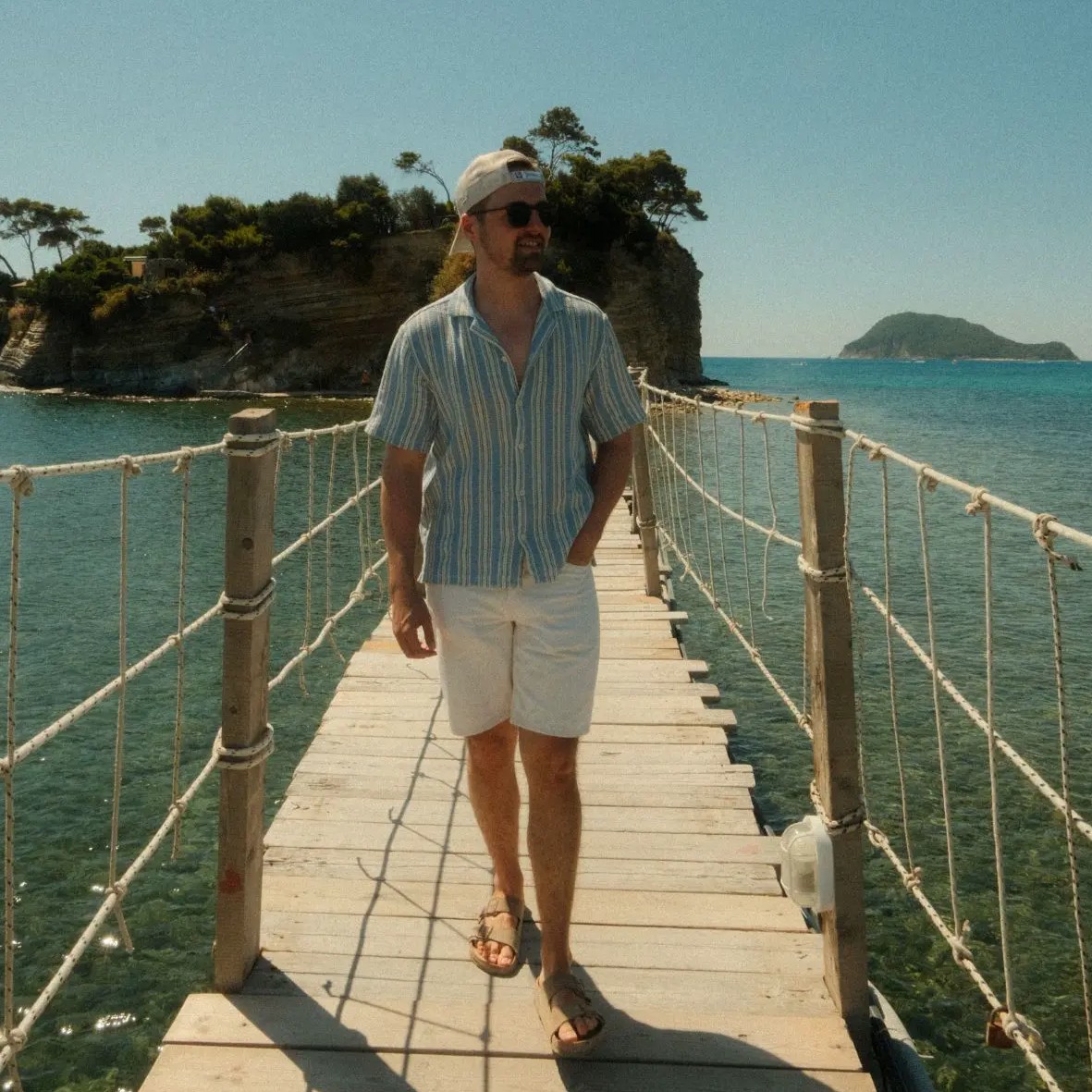 Foto von Christian Rauscher im sommerlichen Outfit auf einer Brücke zu einer Insel im Meer.