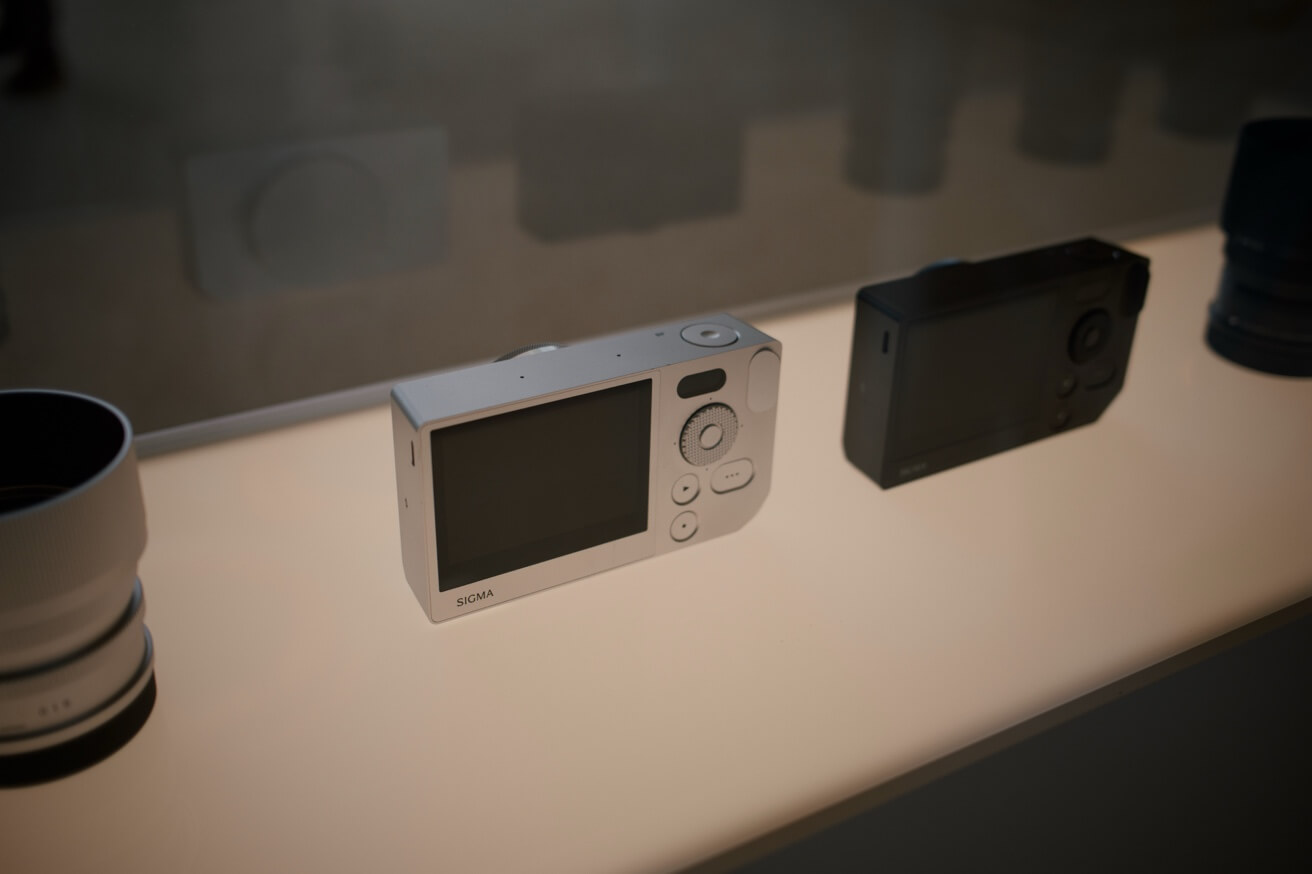 Eine silberne Sigma-Kompaktkamera liegt auf einem hellen Tresen in einer Vitrine.