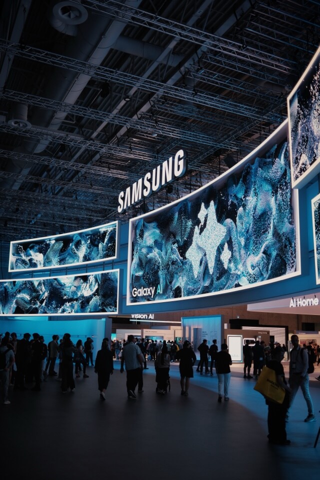 Besucher auf einem großen Samsung-Messestand mit leuchtenden, geschwungenen Bildschirmen.