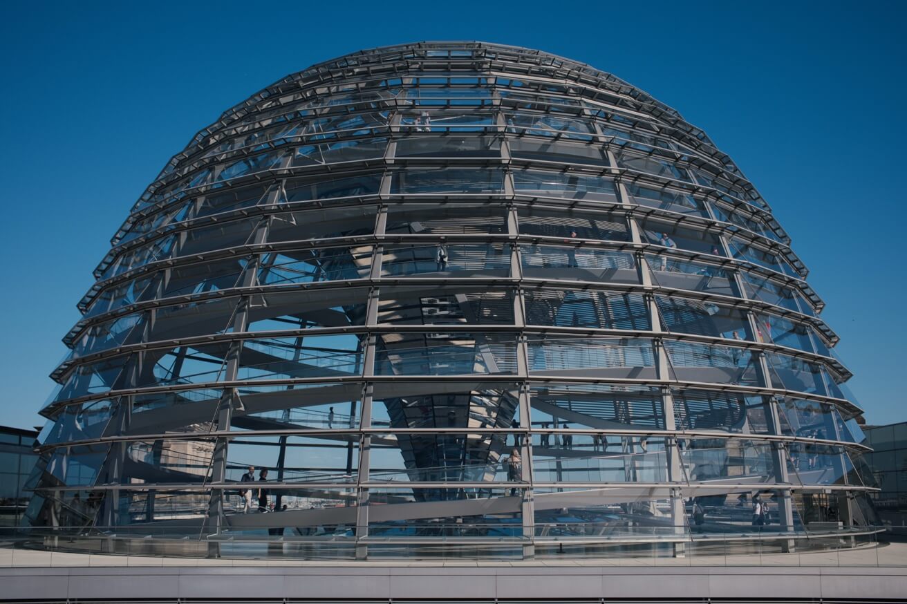 Die große Glaskuppel des Berliner Reichstagsgebäudes von außen gegen einen blauen Himmel.