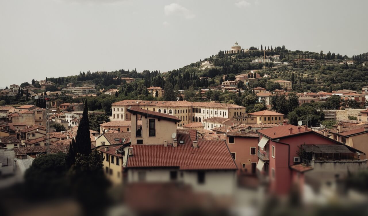 Ein Panoramablick über die Ziegeldächer einer italienischen Stadt auf einen grünen Hügel.