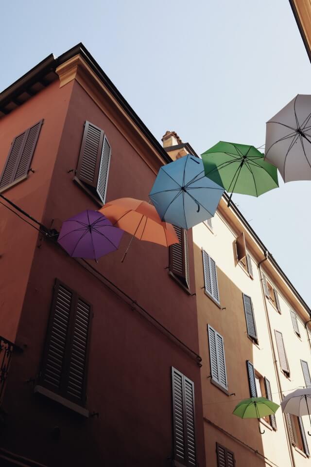 Bunte Regenschirme sind als Dekoration zwischen den Fassaden von zwei Häusern aufgespannt.