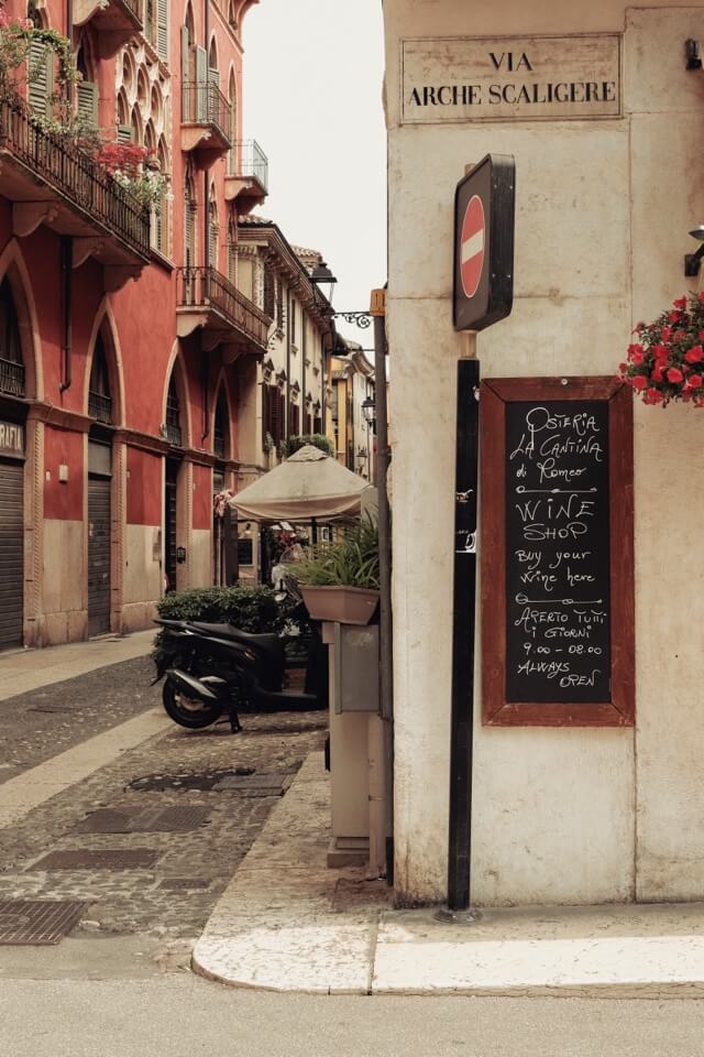 Eine handgeschriebene Tafel für einen Weinladen lehnt an einer Hausecke in einer italienischen Gasse.