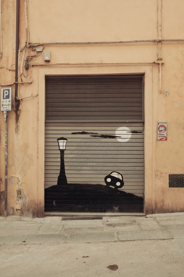 Ein Graffiti mit einer Laterne und einem Auto in einer nächtlichen Landschaft auf einem Rolltor.