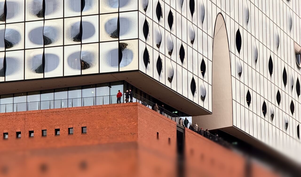 Besucher stehen auf der Aussichtsplattform der Elbphilharmonie, die den Backsteinsockel von der Glasfassade trennt.