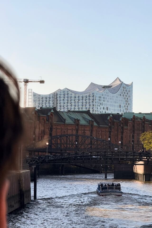 Eine Hafenrundfahrt-Barkasse fährt auf einem Fleet durch die Speicherstadt mit der Elbphilharmonie im Hintergrund.