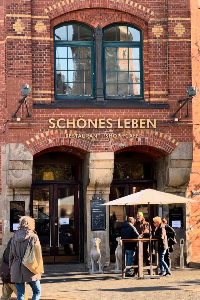 Menschen stehen vor dem Eingang des Restaurants 'Schönes Leben' in einem Backsteingebäude der Speicherstadt.