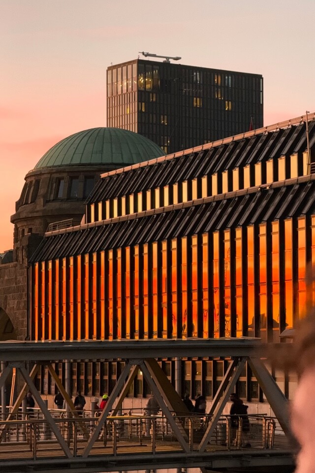 Die Fensterfront eines modernen Gebäudes an den Landungsbrücken reflektiert den orangefarbenen Sonnenuntergang.