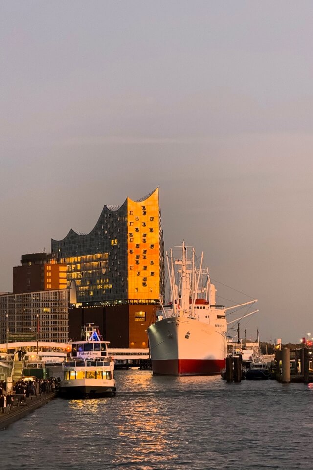 Die Elbphilharmonie und ein weißes Museumsschiff im Hamburger Hafen bei Dämmerung.