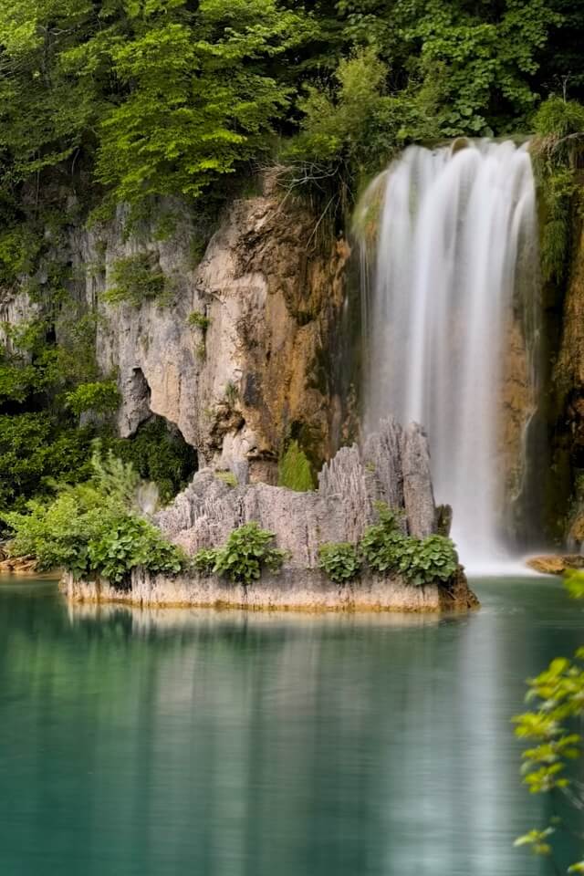 Ein breiter Wasserfall fällt im Nationalpark Plitvicer Seen über eine Felskante in einen türkisen See.