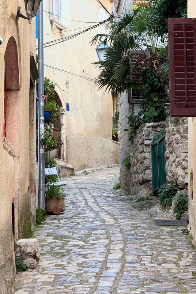 Eine schmale Gasse mit Kopfsteinpflaster führt zwischen alten Steinhäusern hindurch.