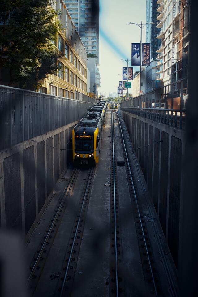 Eine gelbe U-Bahn der E-Line fährt in einem Betongraben durch die Innenstadt von Los Angeles. Auf der Zielanzeige steht 'Go Dodgers!'