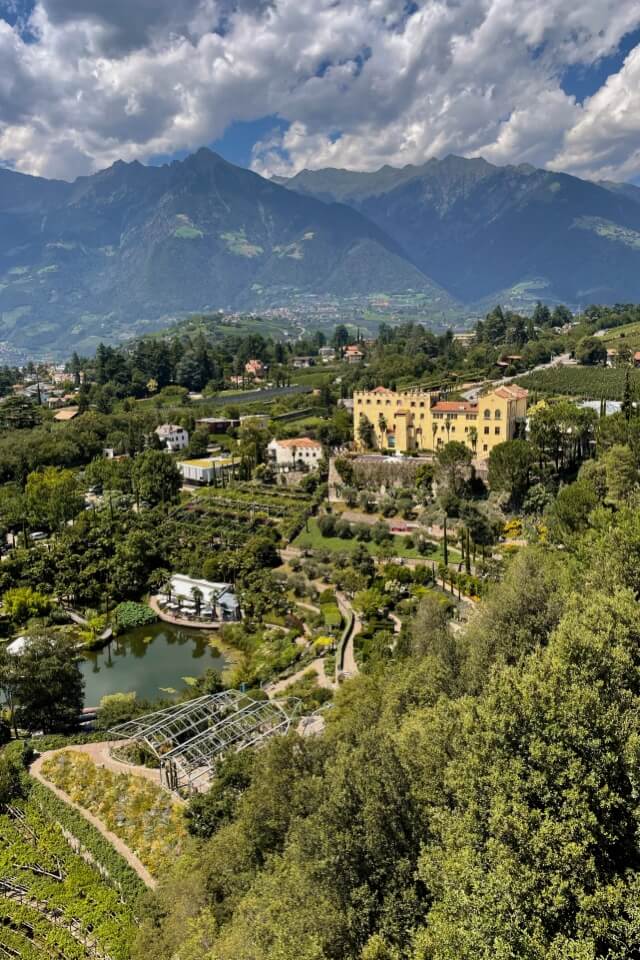 Ein Überblick über die Gärten von Schloss Trauttmansdorff mit dem Schloss und einem Teich.