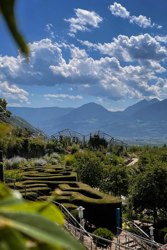 Die Gärten von Schloss Trauttmansdorff mit einem Hecken-Labyrinth und Gewächshäusern vor den Bergen.