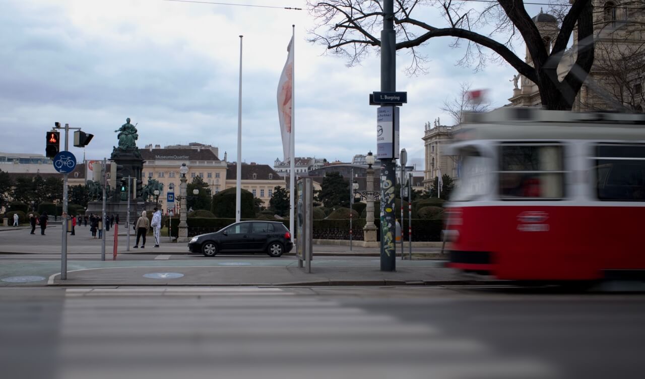 Eine rote Straßenbahn fährt mit Bewegungsunschärfe über eine Kreuzung in der Wiener Innenstadt.