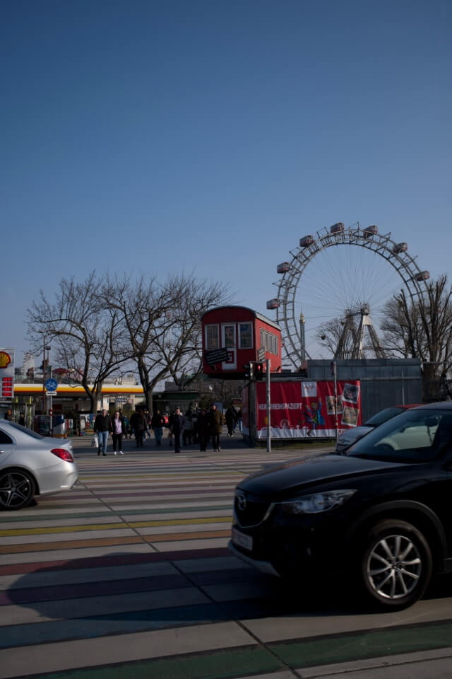 Das Wiener Riesenrad im Prater an einem sonnigen Tag, gesehen über einen bunten Zebrastreifen.