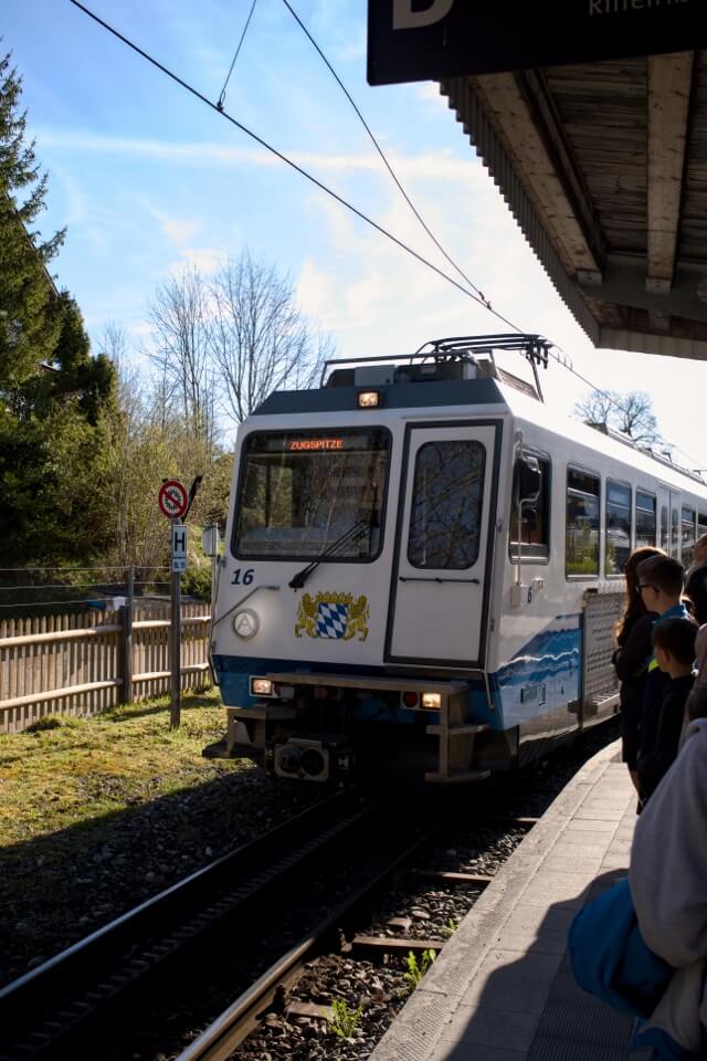 Die weiß-blaue Zahnradbahn mit der Aufschrift Zugspitze fährt an einem Bahnsteig ein.
