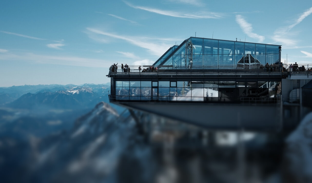 Besucher stehen auf der Aussichtsterrasse der modernen Gipfelstation der Zugspitze und blicken auf die Alpen.