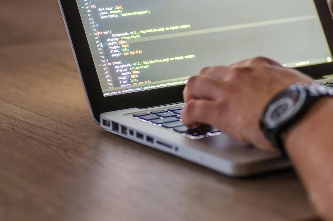 Laptop mit Code und Hand auf Tastatur