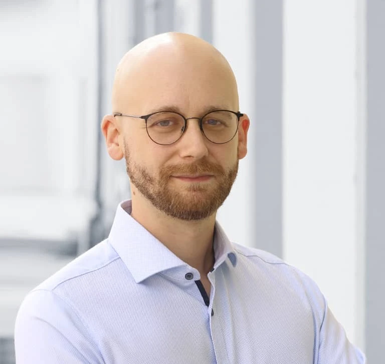 Bild von einem Mann der mit verschränkten Armen und im Hemd in die Kamera blickt.